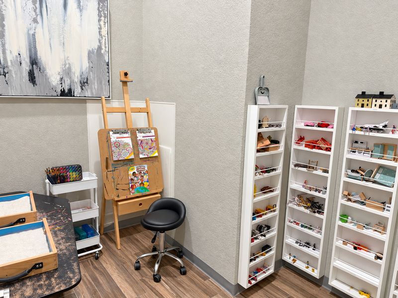 Frisco playroom with sand trays, an art easel, a paint cart and shelves of miniature figures